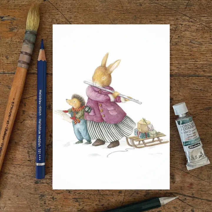 Ansichtkaart Christmas singers van Mhairi Hellbrandt Illustraties met een muziekmakende egel en konijn naast de slee met cadeaus in de sneeuw